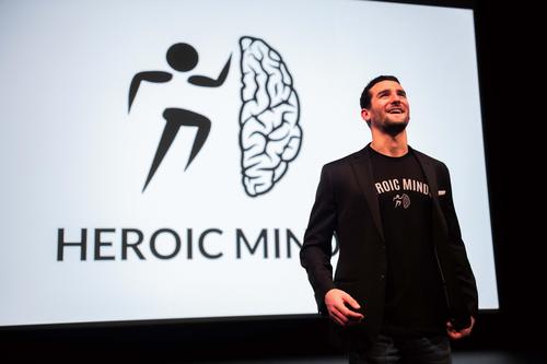 Ben Fanelli speaks on stage with the Heroic Minds logo behind him.