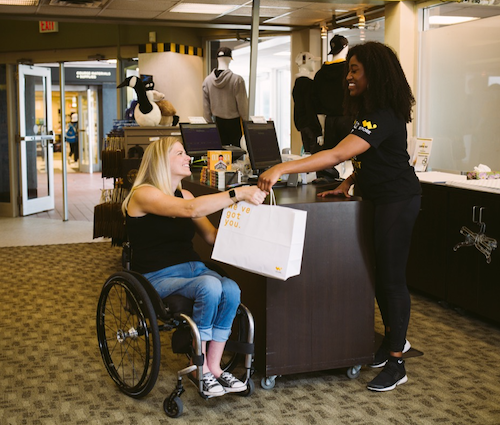 A staff member at the W store hands a bag to a woman in a wheelchair.
