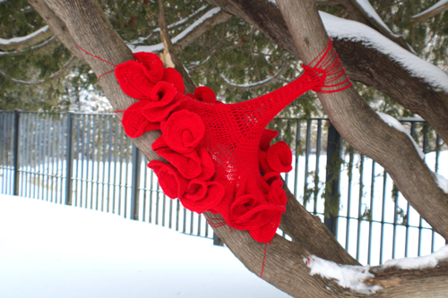 A red crocheted bouquet of flowers wrapped around tree branches.