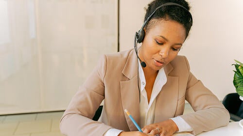 A woman wearing a headset works on paperwork.