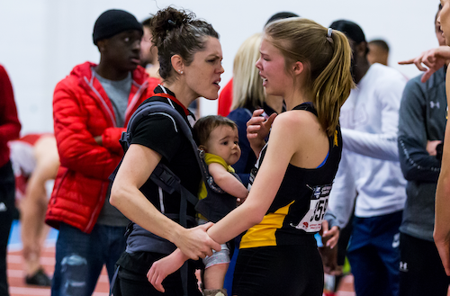 Track &amp; Field Head Coach Kate Bickle-Ferth encourages a student-athlete while wearing a baby in a baby carrier.