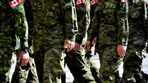 Canadian soldiers in camouflage fatigues on the march, Canadian flag patches on their shoulders.
