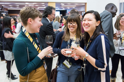 Three Waterloo alumni smile and laugh while holding wine glasses at an alumni chapter event.