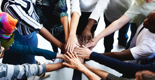 A diverse group of people put their hands together for a cheer.