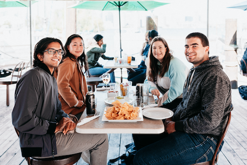 Four young people sit at a table with nachos.