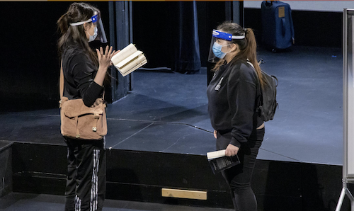 Two actors in masks and face shields rehearse a play on stage.