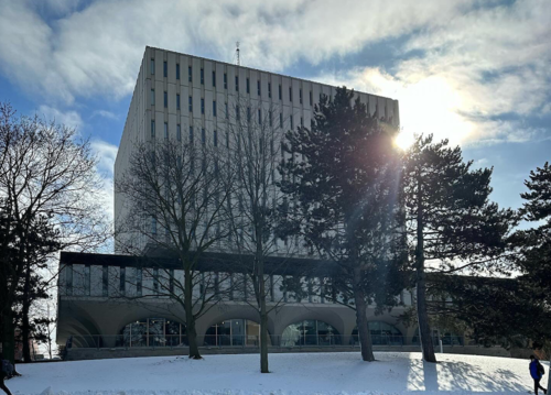 The sun peeks out from behind the Dana Porter library in a winter setting.