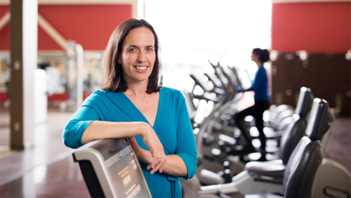 Dr. Laura Middleton stands in front of a row of exercise bikes.