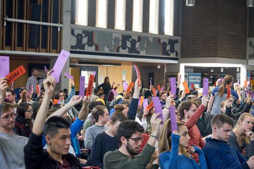 Students raise their hands to vote during a General Meeting.