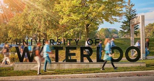 Blurred images of people walking past the University of Waterloo sign at its former location on University Avenue.