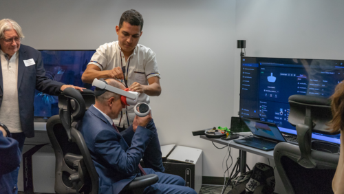 A Games Institute staff member assists a volunteer in putting on a virtual reality headset.