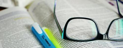 A pen, a highlighter and a pair of eyeglasses sit on the open pages of a book.