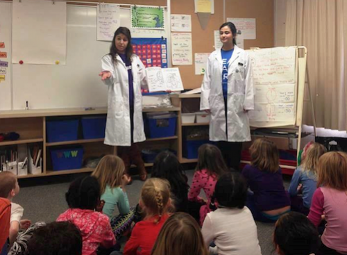 Two Pharmacy volunteers teach in front of grade schoolers.
