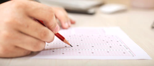 A person fills out an exam with a pencil.