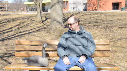 James McCarthy, a GooseWatch specialist, sits with a goose decoy on a park bench.