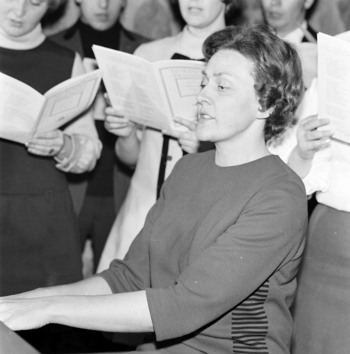 Professor Helen Martens leads a choir while playing piano.