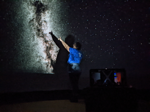 An astronomer points to a projection of the Milky Way from inside the Astro-Bubble.