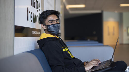 A young man wearing a mask sits in front of a poster that says &quot;change the world.&quot;