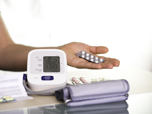 A person holds a blister pack of pills in their hand next to a blood pressure monitoring cuff.
