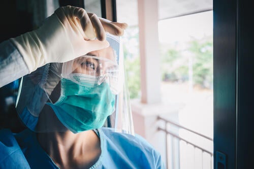 A healthcare working in full PPE takes a moment to catch her breath while looking out a window.
