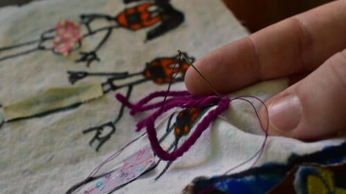 A close-up of a person using a needle to stitch quilt fabric together.