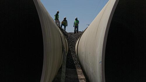 Workers in hard hats stand above two half-buried pipes in the ground