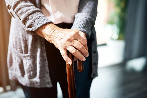 An elderly person's hands rest atop a cane.