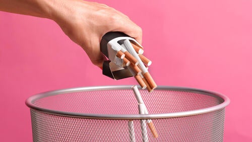 A person throws a pack of cigarettes into a wastebasket.
