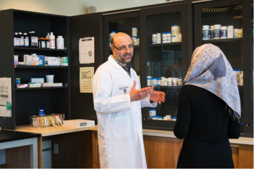 A pharmacy professor speaks with a woman wearing a headscarf.