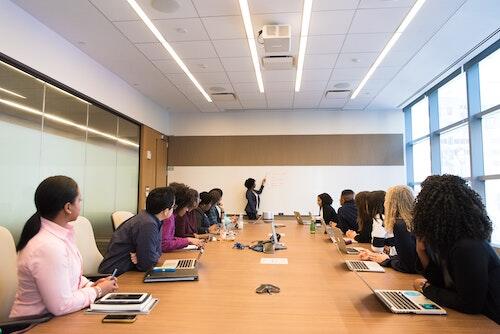 a woman gives a presentation in a boardroom while co-workers look on.