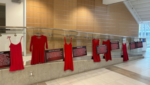 Red Dresses with info placards hang on a railing in the Health Expansion Building.