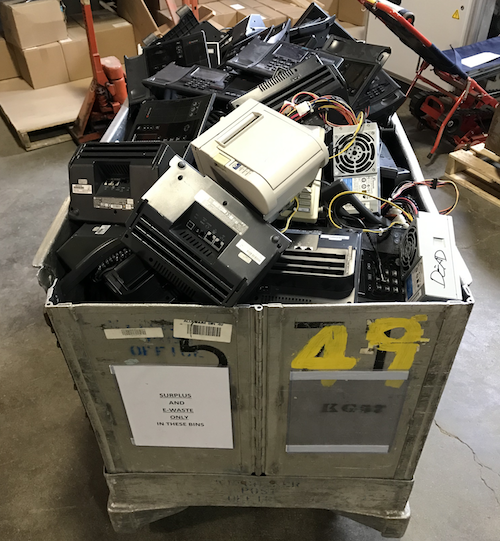 A bin full of discarded e-waste, mostly office phones and printers.