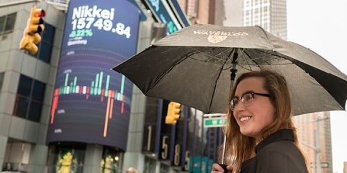 A woman holding a University of Waterloo umbrella in front of a building marquee highlighting the Nikkei stock market index.
