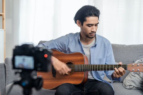A young man plays guitar while seated on a couch.