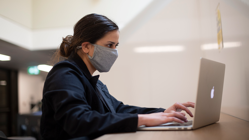 A woman wearing a mask uses a laptop.