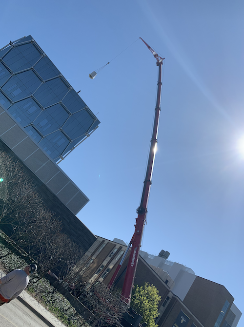 A crane lifts an exhaust fan atop the QNC building.