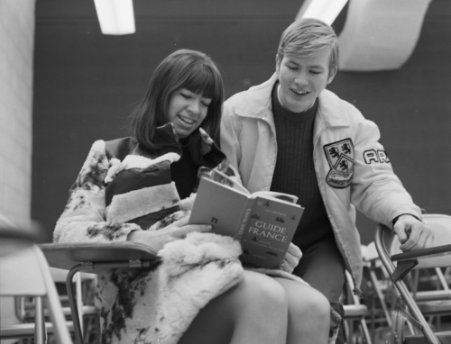 A young woman reads &quot;Guide France&quot; in a fur coat while a young man wears a UW leather jacket and reads over her shoulder in a 1968 photo.