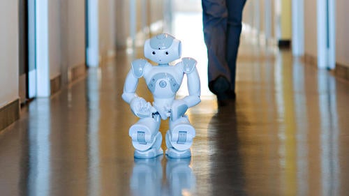 The small humanoid Nao robot stands in a hallway.