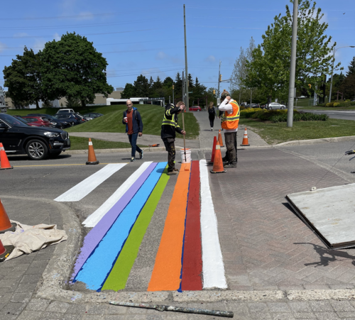 Plant Operations painters use rollers to paint a rainbow crosswalk on the ring road near Columbia Street.