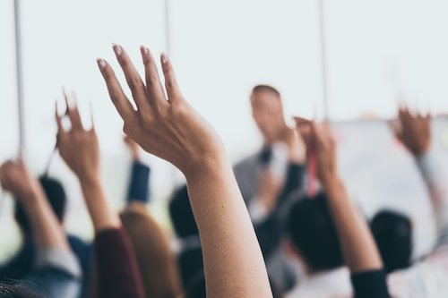 People raising their hands in a classroom setting.
