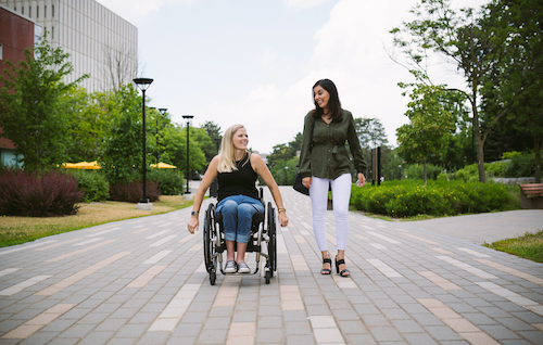 A woman walks next to a woman in a wheelchair outside the Tatham Centre.