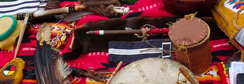  moccasins, drums, eagle feathers, pipes, etc. laid out on a blanket.