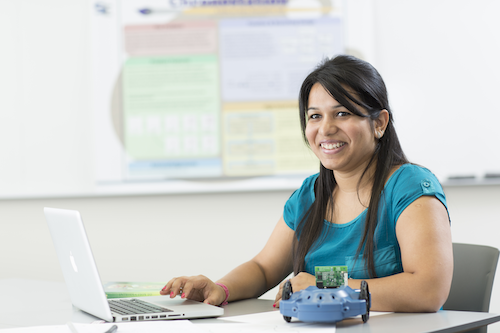 A woman smiles as she works on a laptop.