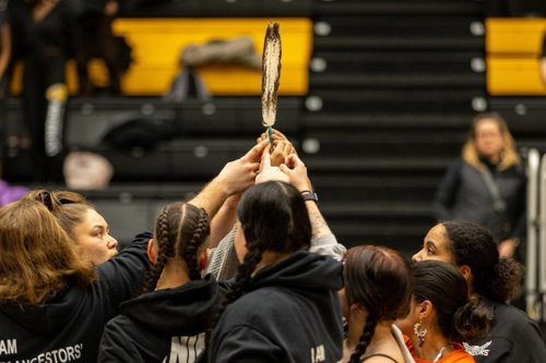 Athletes raise an eagle feather at a sporting event.