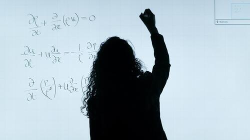 A woman in silhouette writes math equations on a whiteboard.