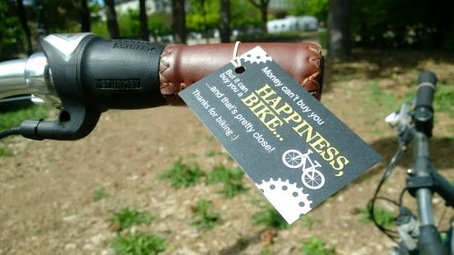 A close-up of a bicycle handlebar with a thank-you note attached.