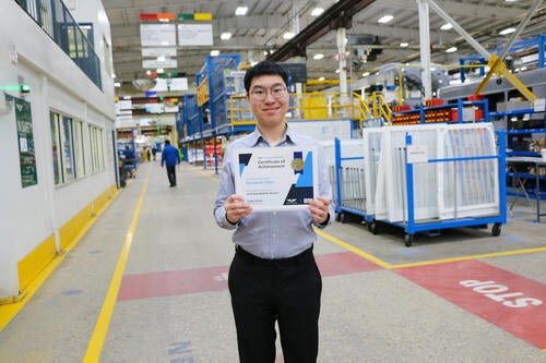 Terrance Chen stands holding a certificate on a factory floor.