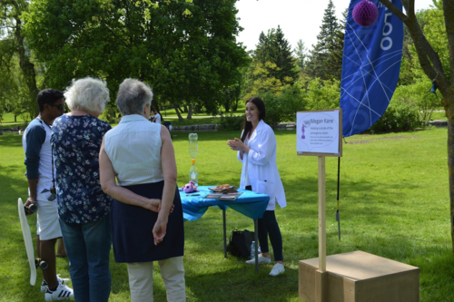 Megan Kane demonstrates scientific principles at her booth in the park while people look on.
