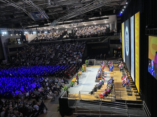 The Convocation stage in the Physical Activities complex lit up with spectators in the audience.