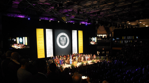 University representatives and special guests stand on the Convocation stage in the Physical Activities Complex.